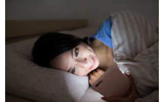 Frau liegt im Bett und checkt ihr Smartphone