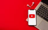 Symbolbild zeigt ein Smartphone mit einem YouTube-Logo, das auf einem aufgeklappten Notebook liegt